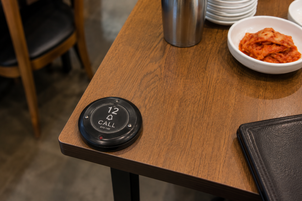 Why Do Koreans Press a Bell Instead of Calling a Waiter? A round call button labeled Table 12 attached to the corner of a table in a Korean restaurant.