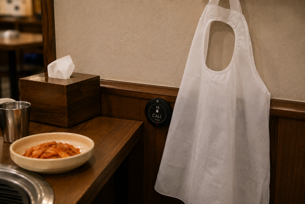 Why Do Koreans Press a Bell Instead of Calling a Waiter? A restaurant call button partially hidden behind a disposable apron in a Korean BBQ restaurant.